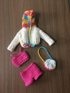 a crocheted doll outfit and hat on a wooden table next to it's accessories