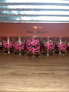 four glasses with pink lettering on them sitting on a table next to a toaster