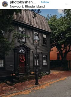 a black house with two windows and a red door on the side walk in front of it