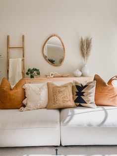 a living room filled with lots of pillows on top of a white couch next to a mirror