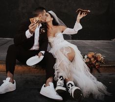 a bride and groom sitting on the ground eating pizza