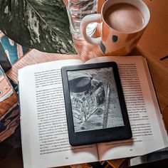 an open book sitting on top of a table next to a cup of coffee