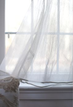 a white curtain hanging over a window sill next to a pillow on a bed