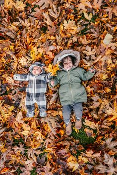 two babies laying in leaves on the ground with their faces close to each other and looking up