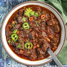 a bowl filled with meat and vegetables on top of a blue table cloth next to a spoon