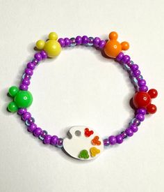 Perfect for Festival Of The Arts! This beaded stretch bracelet with purple glass seed beads and plastic mouse ears in an array of colors to match the adorable painters palette with tiny mouse ear paint splatters.  Bracelets are available in a variety of lengths.  Pick your custom length from the drop down menu below.  Please be aware that beading may slightly differ from what is pictured as to accommodate selected sizing.  All our bracelets are made with quality in mind.  With that being said, a Adjustable Multicolor Novelty Craft Supplies, Art Bracelet, Painters Palette, Paint Splatters, Purple Glass, Mouse Ears, Beaded Stretch Bracelet, The Arts, Stretch Bracelet