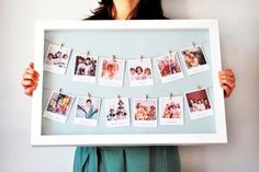 a woman holding up a white frame with photos hanging on it