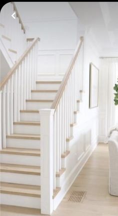 a living room filled with furniture and a white stair case next to a tree in a vase