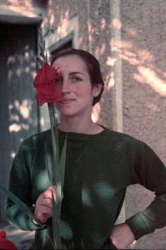 a woman holding a flower in front of her face while standing next to a building