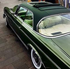 an old green car is parked on the side of the road in front of other cars