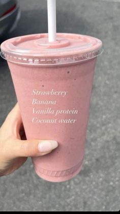 a hand holding a pink smoothie with a straw in it