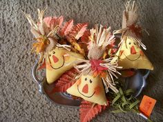 three scarecrows are sitting in a bowl with autumn leaves on the floor next to it