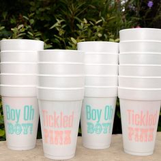 six white cups with pink, blue and green lettering are lined up on a table