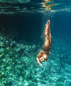 a man swimming in the ocean with his back turned to the camera and diving under water