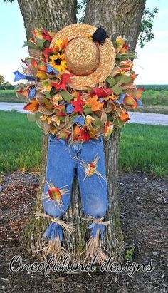 a scarecrow wearing jeans and a straw hat is standing in front of a tree