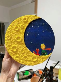 a person holding up a yellow and blue painted moon