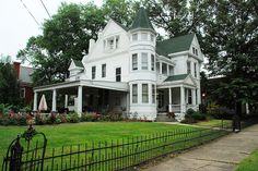 a large white house sitting on top of a lush green field next to a fence