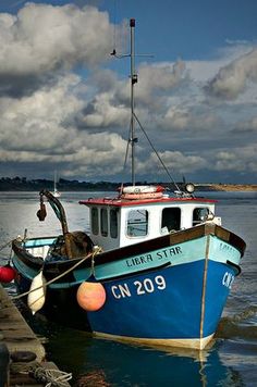 a blue and white boat is docked at the dock with clouds in the sky above