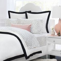 a white bed with black trim and polka dots on the comforter is next to a pink lamp