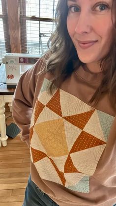 a woman standing in front of a window wearing a brown shirt and jeans with an orange geometric design on it