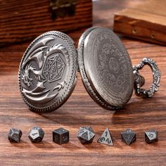 a silver pocket watch with seven dice pieces around it on a wooden table next to other items