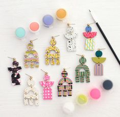 some colorful earrings are laying on a table next to paintbrushes and an artist's palette