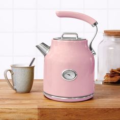 a pink tea kettle sitting on top of a wooden table next to a mug and cookies