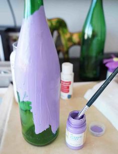 the paint is being used to make an art project with purple and green bottles in the background