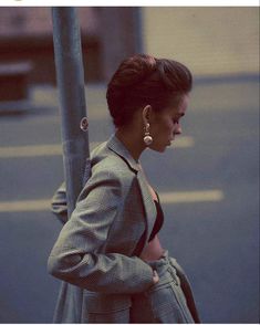 a woman is walking down the street with her hand in her pocket and holding onto a pole