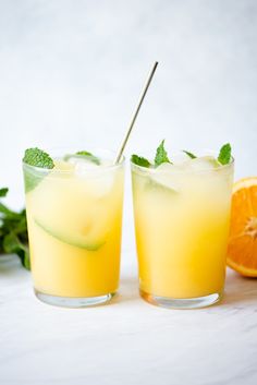 two glasses filled with orange juice and cucumber garnish