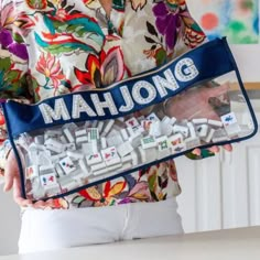 a woman holding a bag with the word mahjong printed on it in front of her