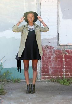 a woman in a black dress and green jacket with a hat on top of her head