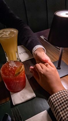 two people sitting at a table with drinks in front of them, one holding the other's hand