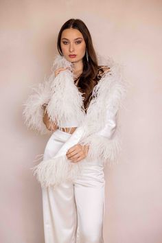 a woman in white is posing with her hands on her hips and wearing a feathered jacket