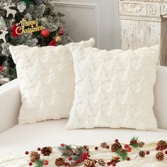 two white pillows sitting on top of a couch next to a christmas tree with pine cones