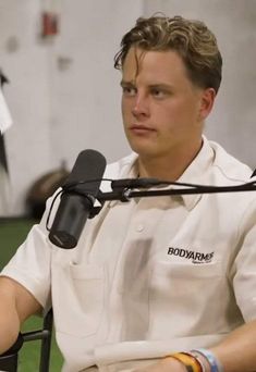 a man sitting at a table with a microphone in front of him and wearing a white shirt