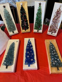 five small christmas trees are displayed in wooden frames on a red tablecloth with white snowflakes