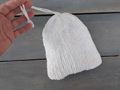 a hand holding a white knitted bag on top of a wooden table next to a string