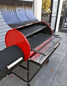 a red and black bbq grill sitting on top of a metal cart next to a building