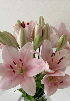 a glass vase filled with pink flowers on top of a white table next to a wall