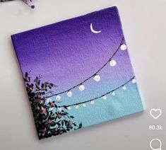 a purple and blue painting with string lights hanging from it's sides on a white table