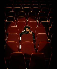 a woman sitting in an empty auditorium with her head resting on the back of a red chair