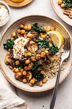 a white plate topped with rice, mushrooms and spinach next to lemon wedges