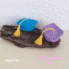 two crocheted graduation caps sitting on top of a piece of drifty wood