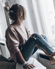 a woman sitting on top of a bed next to a window with her legs crossed