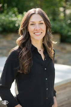 a woman standing in front of a wooden bench smiling at the camera with her hands on her hips