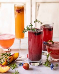 three glasses filled with different types of drinks on a table next to fruit and herbs