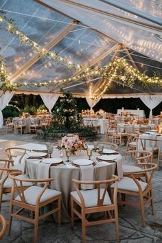 tables and chairs are set up under a tent for an outdoor wedding reception with lights strung from the ceiling