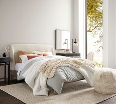 a bedroom with white walls and wood flooring has a large bed covered in an overstuffed blanket