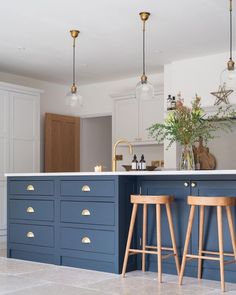 two stools sit in front of an island with marble countertops and blue cabinets